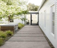 a walkway leading to a white house with black doors and windows by an open door