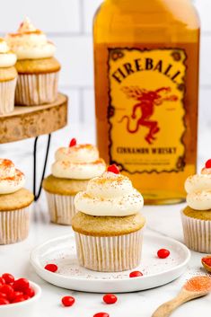 cupcakes with white frosting and red berries next to a bottle of fireball