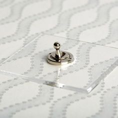 a metal button on top of a clear glass plate with white and silver designs in the background