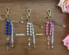 three key chains with beads and charms hanging from them on a wooden table next to flowers