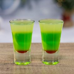 two shot glasses filled with green and red liquid sitting on a wooden table next to each other