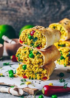 three burritos stacked on top of each other with peas and peppers around them