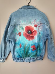 a painted denim jacket with red flowers on it hanging from a hanger against a wall