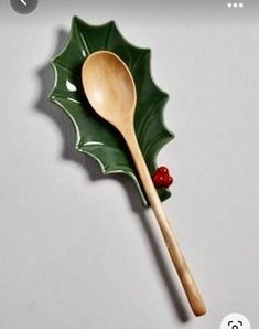 a wooden spoon sitting on top of a green leaf shaped plate with a red berry