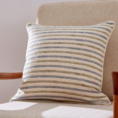 a striped pillow sitting on top of a chair next to a wooden armrest and table