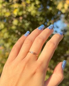 a woman's hand with blue nail polish and a ring on her finger, in front of some trees