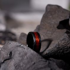 a wedding band with an orange and black stripe sits on top of some rocks in the sun