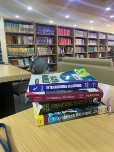 a stack of books sitting on top of a wooden table in front of a library