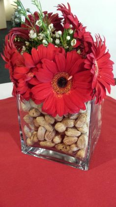 a square vase filled with red flowers and nuts