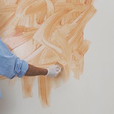 a man in blue shirt and white gloves painting a wall with orange paint on it