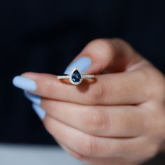 a woman's hand holding a ring with a pear shaped blue diamond on it