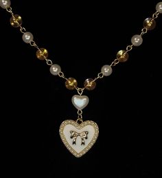 The piece combines 6mm beads: clear with golden sparkles and white pearlescent, alternating for a delicate shimmer. At it's heart lies a heart shaped pearlescent bead, with a dainty heart shaped pendant handing below, adorned with a gold bow framed by tiny pearls. All the beads are connected with a gold toned wire and incudes an extension chain for adjustable length, secured with a lobster claw clamp. White Heart Beads Jewelry For Party, Dainty White Pearl Heart Necklace, White Pearl Heart Necklace With Pearl Charm, Elegant Heart-shaped Jewelry With Gold Beads, White Dainty Heart Necklace With Pearl Chain, Gold Heart Beads Necklace For Party, Dainty White Heart Necklace With Pearl Chain, White Heart Necklace For Valentine's Day Party, Valentine's Day White Heart Necklace For Party