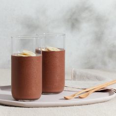 two glasses filled with chocolate and bananas on a plate