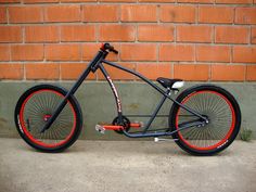 a black bike with red rims parked in front of a brick wall on the sidewalk