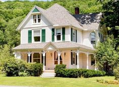 a large white house with green shutters in the front yard and trees around it