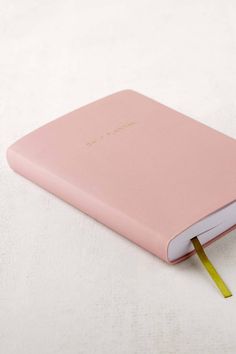 a pink notebook with a yellow tape sticking out of the cover on a white surface