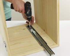 a person is using a drill to attach the bottom part of a wooden cabinet door