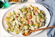 a white plate topped with pasta salad next to a glass of water and a wooden spoon