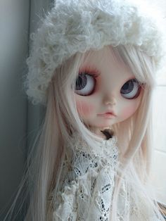 a doll with long white hair and big eyes wearing a fur hat on top of her head