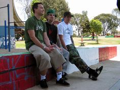 three men sitting on a wall with their feet up and one man in green shirt