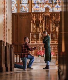 two people kneeling down in front of a stained glass church window, one holding his hand up to the other's chest