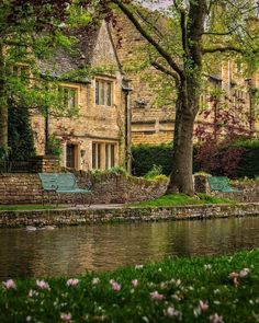 two green park benches sitting next to a body of water in front of a house