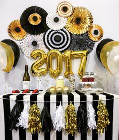 a black and white striped table with gold foil balloons, streamers and tassels