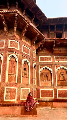 a woman sitting on a bench in front of a building with intricately carved walls