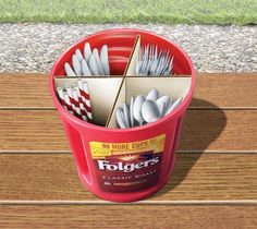 a red bucket filled with silverware on top of a wooden table next to grass