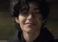 a young man with curly hair smiling and wearing a black hoodie in front of a building