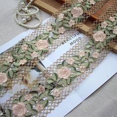 an open book with lace and flowers on it next to a beaded chain necklace