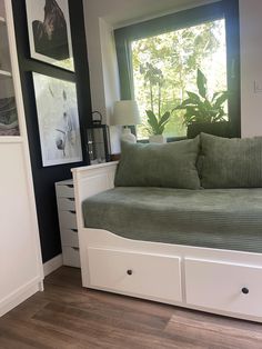 a white daybed with drawers underneath it in front of a window and pictures on the wall