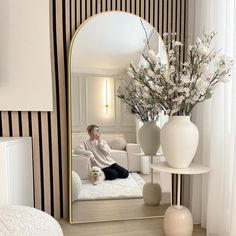 a woman sitting on a couch in front of a mirror with flowers and vases