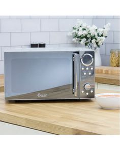 a silver microwave oven sitting on top of a wooden counter next to a bowl and plate