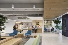 people are standing in the lobby of an office with blue chairs and wooden benches on the floor