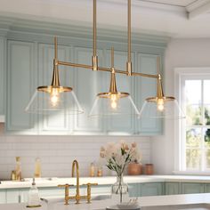 a kitchen with blue cabinets and white countertops, gold fixtures and pendant lights over the island