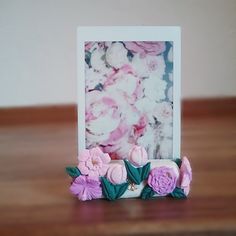 a photo frame sitting on top of a wooden table next to pink and white flowers