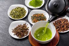 a tea pot being filled with green tea surrounded by white plates and spoons on a black table