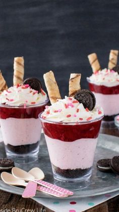 three dessert cups with oreo cookies on top and red liquid in the middle, topped with whipped cream and sprinkles