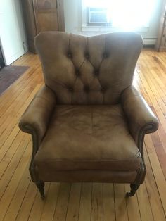 a brown leather chair sitting on top of a hard wood floor next to a window