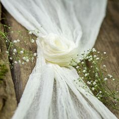 a white scarf with flowers on it sitting on a wooden table next to a piece of cloth