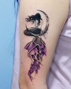 a woman's arm with a tattoo on it that has a mermaid sitting on the moon