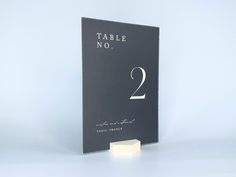 the table number is two in white lettering on a black book cover with a block of wood next to it