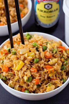 two bowls filled with rice, peas and carrots next to a bottle of beer