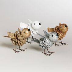 three metal birds are standing next to each other on a white surface with pine cones