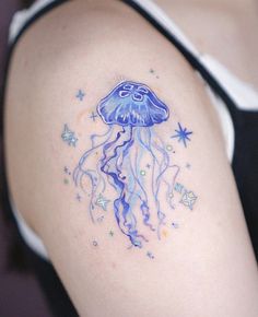 a woman's arm with a blue jellyfish tattoo on it and stars in the background