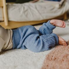 a baby laying on the floor wearing a blue sweater and tan pants with his feet up