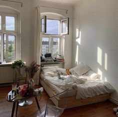 a bed sitting in the middle of a living room next to two windows with lots of sunlight coming through them