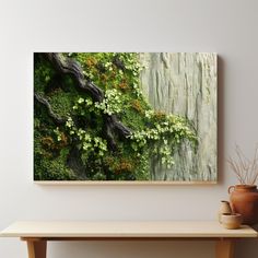 a painting on the wall above a table with a vase and potted plant next to it