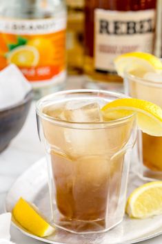 two glasses filled with ice and lemons on a plate